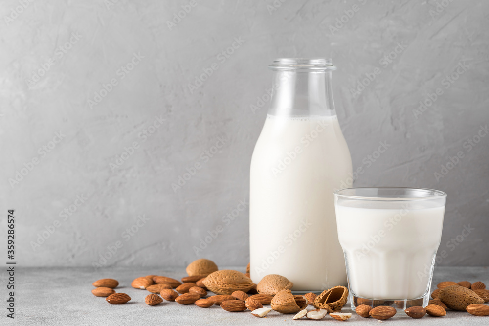 Almond milk in a bottle with glass and almond nuts on concrete background. Vegan dairy free plant milk Almond milk in a bottle with glass and almond nuts on concrete background. Vegan dairy free plant milk
