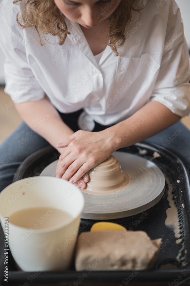 Girl makes pottery from clay. She making ceramic products from white clay using twisted potter's wheel. Girl makes pottery from clay. She making ceramic products from white clay using twisted potter's wheel.