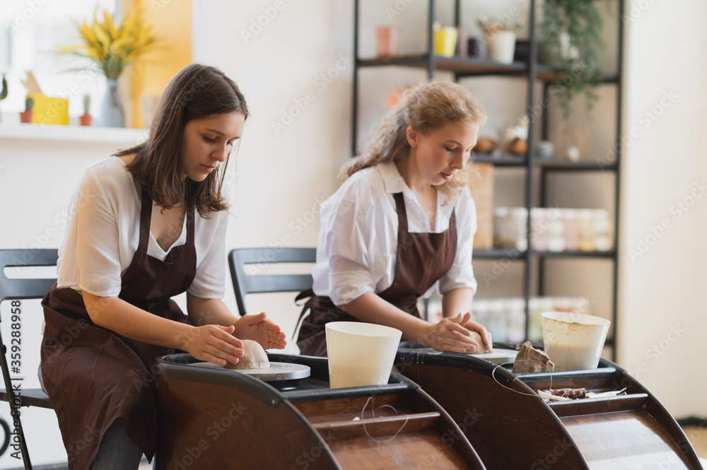 Two female ceramic artists in apron using clay material working in potter studio. Evening freelance distance learning. Adult hobby adventure. Winter educating leisure. Training in modern workshop. Two female ceramic artists in apron using clay material working in potter studio. Evening freelance distance learning. Adult hobby adventure. Winter educating leisure. Training in modern workshop.