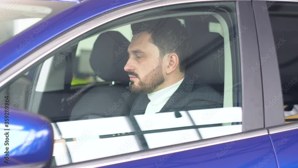 Stylish man sitting in car salon. Young confident guy choosing automobile in showroom Stylish man sitting in car salon. Young confident guy choosing automobile in showroom