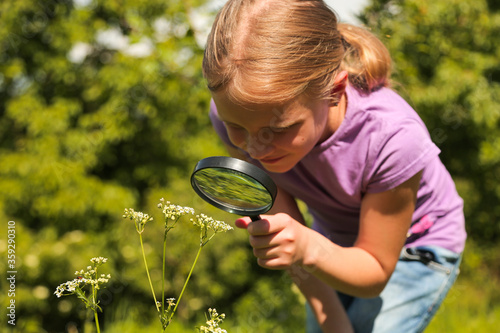 Little girl child looking through a magnifying glass. Closeup portrait on nature. 