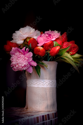 Bouquet of peonies with strawberries. Strawberry bouquet in a vase of natural linen