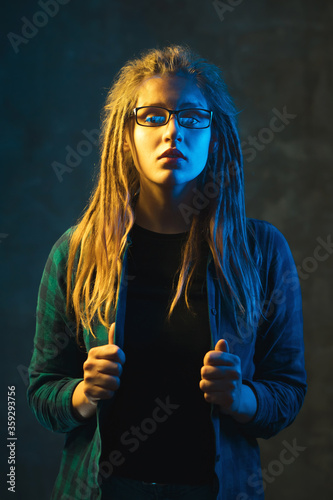 Young woman with dreadlocks in colorful neon lighting. Stylish attractive girl in glasses on dark background.