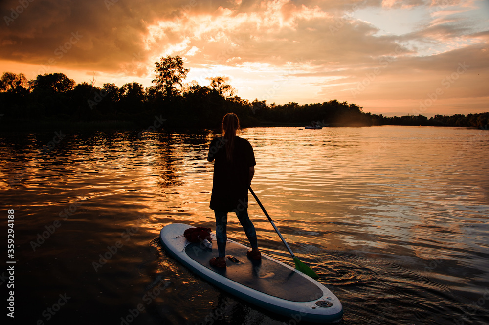 rear view of girl on sup board who floating on the river at sunset