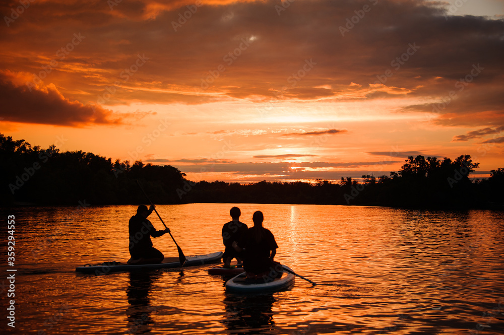 rear view on group of people on sup boards with paddles floating on the river at sunset. rear view on group of people on sup boards with paddles floating on the river at sunset.