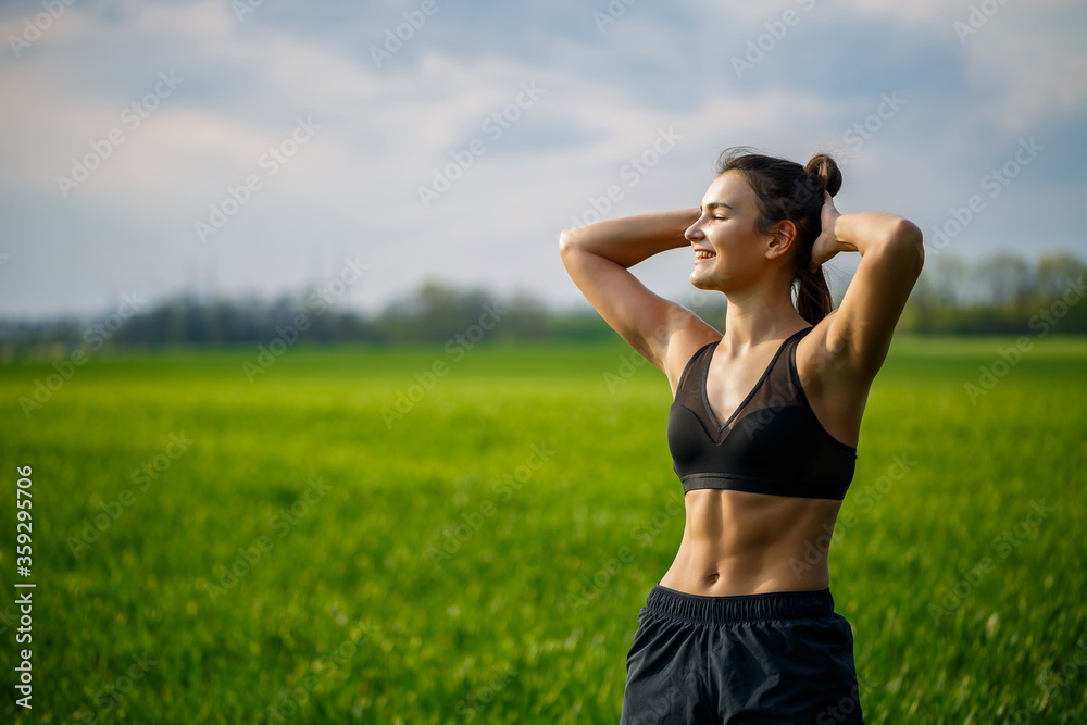 Healthy lifestyle concept. Young attractive woman in sportswear makes stretching her hand before training on the nature at dawn. Muscle warming
