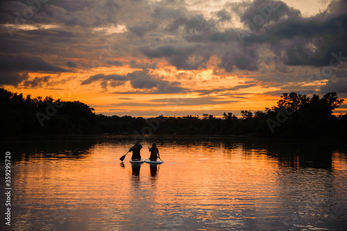 great view of horizon and sunset and river on which pair of people swim on the sup boards © fesenko