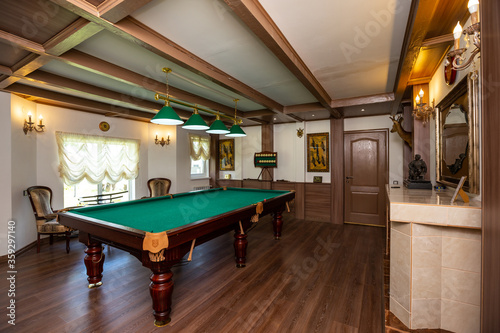 Billiard room interior. Green table for game. Old german style design. Brown wooden decor on the ceiling, walls and floor.