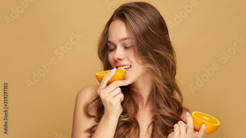 Young beautiful woman holding slices of orange in front of her eyes