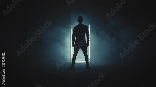 Silhouette of young man standing in the dark smoky room with white light