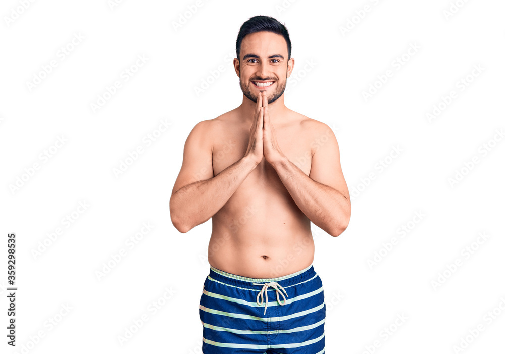 Fototapeta premium Young handsome man wearing swimwear praying with hands together asking for forgiveness smiling confident.