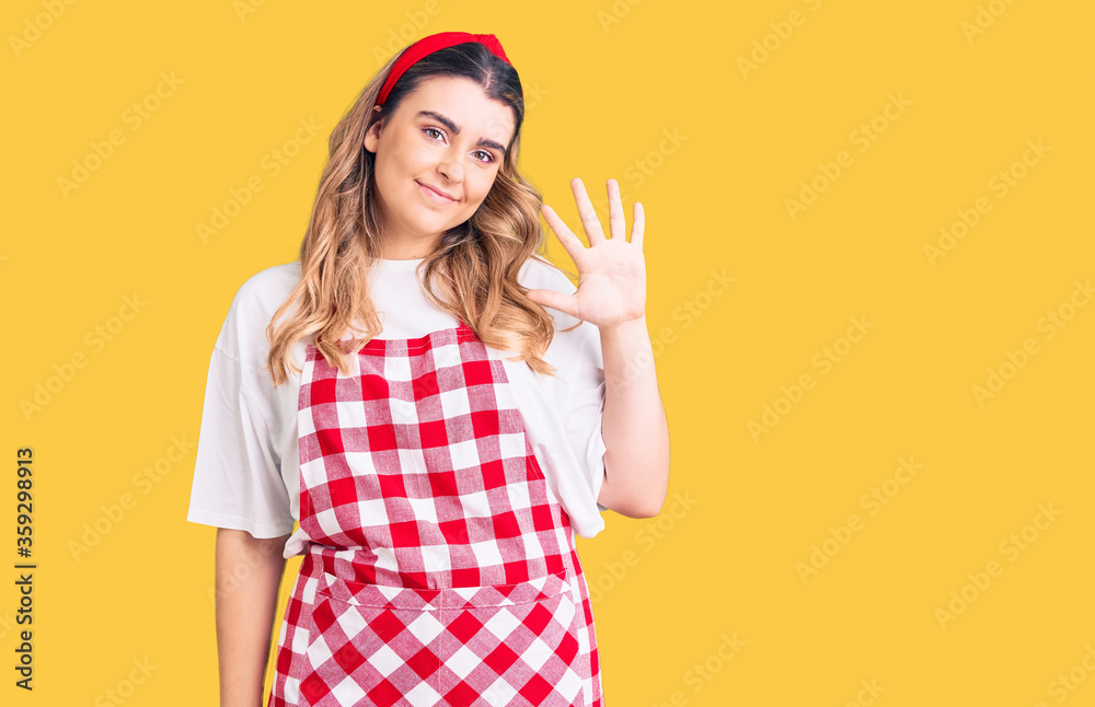 Young caucasian woman wearing apron showing and pointing up with fingers number five while smiling confident and happy. Young caucasian woman wearing apron showing and pointing up with fingers number five while smiling confident and happy.