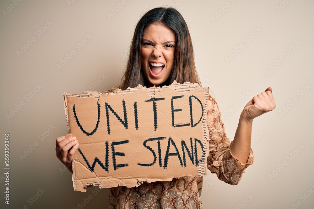 Young beautiful brunette woman asking for union holding banner with unity message screaming proud and celebrating victory and success very excited, cheering emotion Young beautiful brunette woman asking for union holding banner with unity message screaming proud and celebrating victory and success very excited, cheering emotion