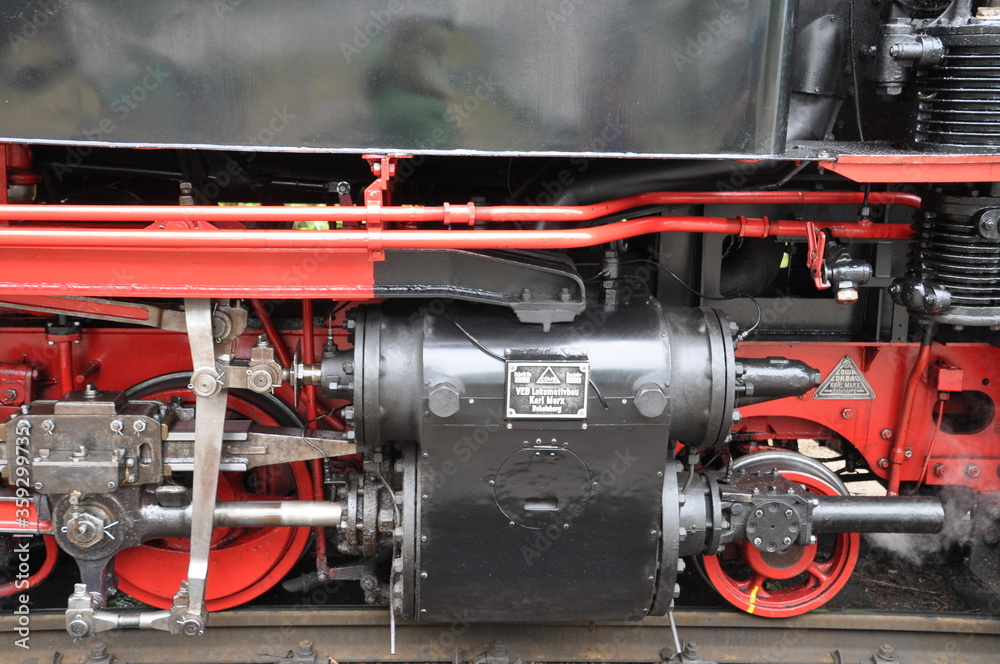 rote Antriebsräder mit Pleuelstangen einer alten Dampflok und austretendem Dampf
