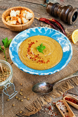 Red lentil cream soup with pepper, spices and parsley in a bowl on napkin and wooden background.