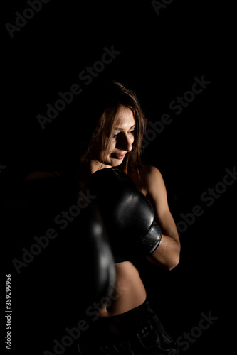 Female boxer training in the dark ring. Silhouette. Boxing concept. Fighter woman fist close up. Sexy girl with perfect body in boxing gloves at gym. concept of health and sport. © MONIUK ANDRII