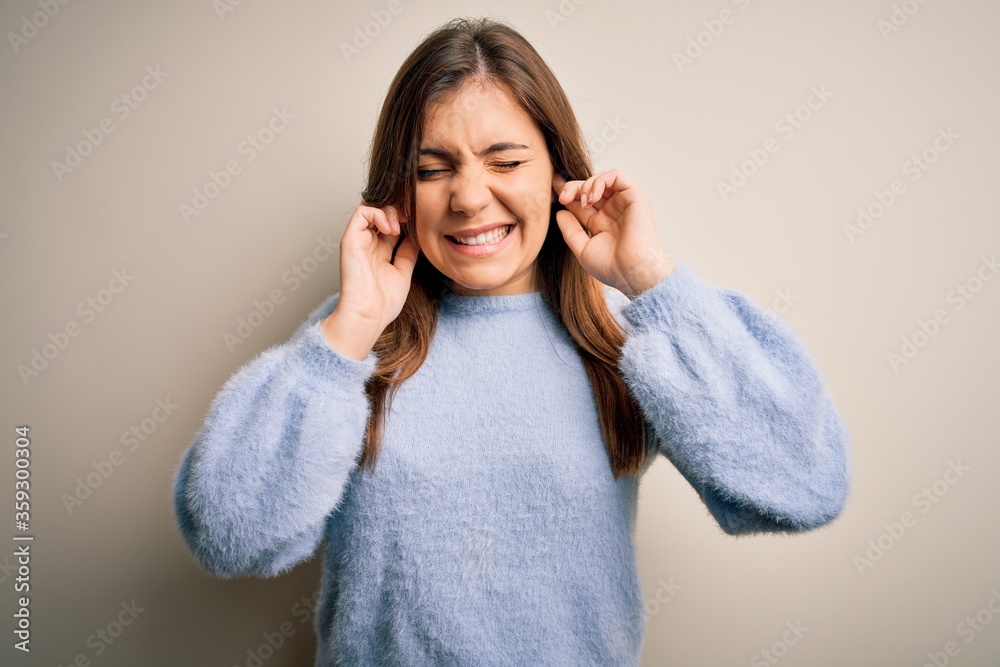 Beautiful young woman wearing casual winter sweater standing over isolated background covering ears with fingers with annoyed expression for the noise of loud music. Deaf concept. Beautiful young woman wearing casual winter sweater standing over isolated background covering ears with fingers with annoyed expression for the noise of loud music. Deaf concept.