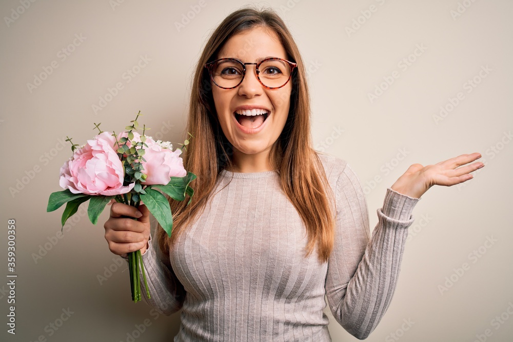 Young blonde woman holding beautiful romantic floral bouquet over isolated background very happy and excited, winner expression celebrating victory screaming with big smile and raised hands Young blonde woman holding beautiful romantic floral bouquet over isolated background very happy and excited, winner expression celebrating victory screaming with big smile and raised hands