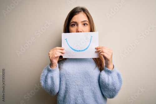 Young blonde woman holding funny smile drawing on mouth as happy expression with a confident expression on smart face thinking serious