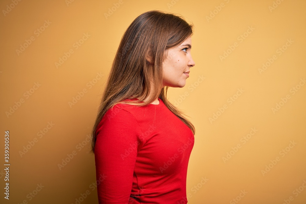 Beautiful young woman wearing casual red t-shirt over yellow isolated background looking to side, relax profile pose with natural face with confident smile. Beautiful young woman wearing casual red t-shirt over yellow isolated background looking to side, relax profile pose with natural face with confident smile.