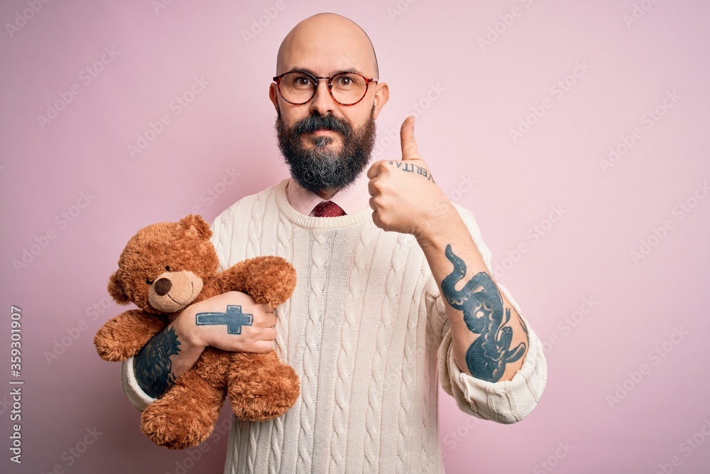 Handsome bald man with beard and tattoo holding teddy bear over ...