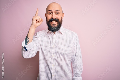 Handsome bald man with beard wearing elegant shirt over isolated pink background pointing finger up with successful idea. Exited and happy. Number one.