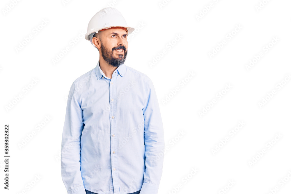 Young handsome man wearing architect hardhat looking away to side with smile on face, natural expression. laughing confident. Young handsome man wearing architect hardhat looking away to side with smile on face, natural expression. laughing confident.