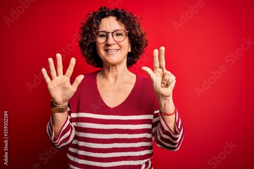 Middle age beautiful curly hair woman wearing casual striped sweater over red background showing and pointing up with fingers number eight while smiling confident and happy.