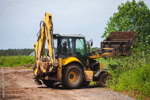 Yellow excavator unloads cargo on the grass. Clearing land from trees, turf and debris