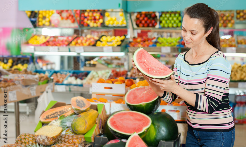 Fototapeta premium Positive Caucasian female choosing fresh fruits at shop