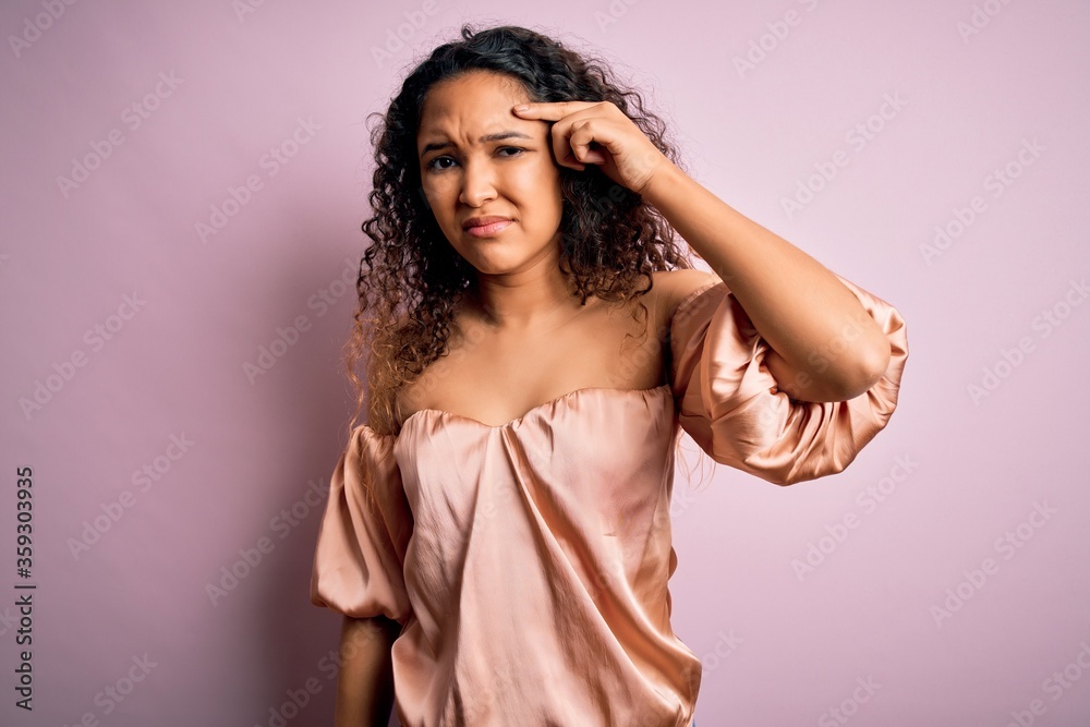 Young beautiful woman with curly hair wearing casual t-shirt standing over pink background pointing unhappy to pimple on forehead, ugly infection of blackhead. Acne and skin problem Young beautiful woman with curly hair wearing casual t-shirt standing over pink background pointing unhappy to pimple on forehead, ugly infection of blackhead. Acne and skin problem