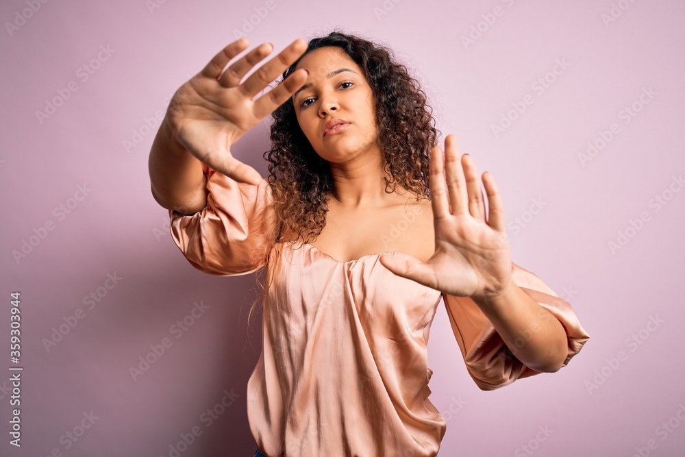 Young beautiful woman with curly hair wearing casual t-shirt standing over pink background doing frame using hands palms and fingers, camera perspective Young beautiful woman with curly hair wearing casual t-shirt standing over pink background doing frame using hands palms and fingers, camera perspective