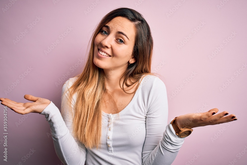 Young beautiful blonde woman with blue eyes wearing white t-shirt over pink background clueless and confused expression with arms and hands raised. Doubt concept. Young beautiful blonde woman with blue eyes wearing white t-shirt over pink background clueless and confused expression with arms and hands raised. Doubt concept.
