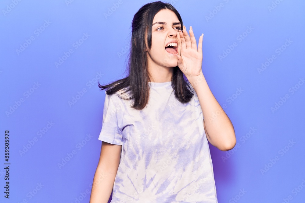 Young beautiful girl wearing casual t shirt shouting and screaming loud to side with hand on mouth. communication concept. Young beautiful girl wearing casual t shirt shouting and screaming loud to side with hand on mouth. communication concept.