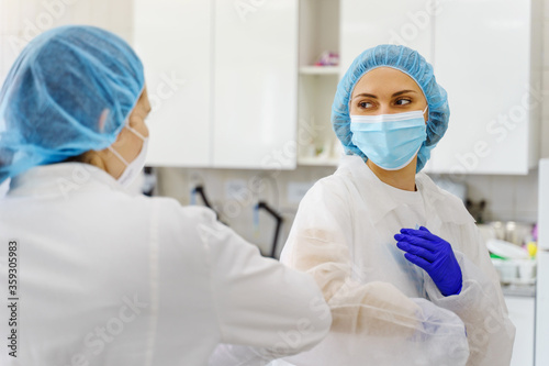 Two women wearing protective equipment bouffant mob cap and protective mask - Elbow bump greeting at hospital or laboratory new normal due to corona virus pandemic spread - support and safety concept