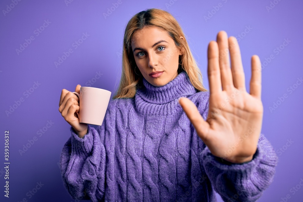 Young beautiful blonde woman drinking cup of coffee over isolated purple background with open hand doing stop sign with serious and confident expression, defense gesture Young beautiful blonde woman drinking cup of coffee over isolated purple background with open hand doing stop sign with serious and confident expression, defense gesture