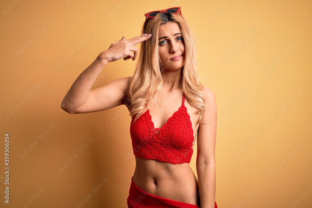 Young beautiful blonde woman on vacation wearing bikini over isolated yellow background Shooting and killing oneself pointing hand and fingers to head like gun, suicide gesture. Young beautiful blonde woman on vacation wearing bikini over isolated yellow background Shooting and killing oneself pointing hand and fingers to head like gun, suicide gesture.