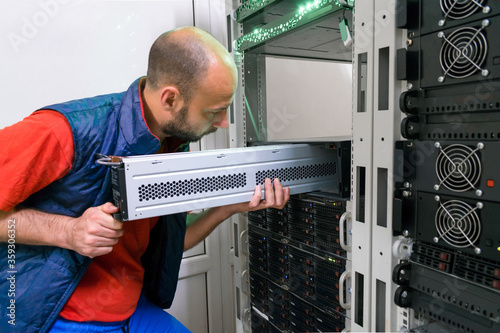 The man installs a new battery into the uninterruptible power supply. Replacing the power module in the server room rack. Maintenance of data center equipment. photo
