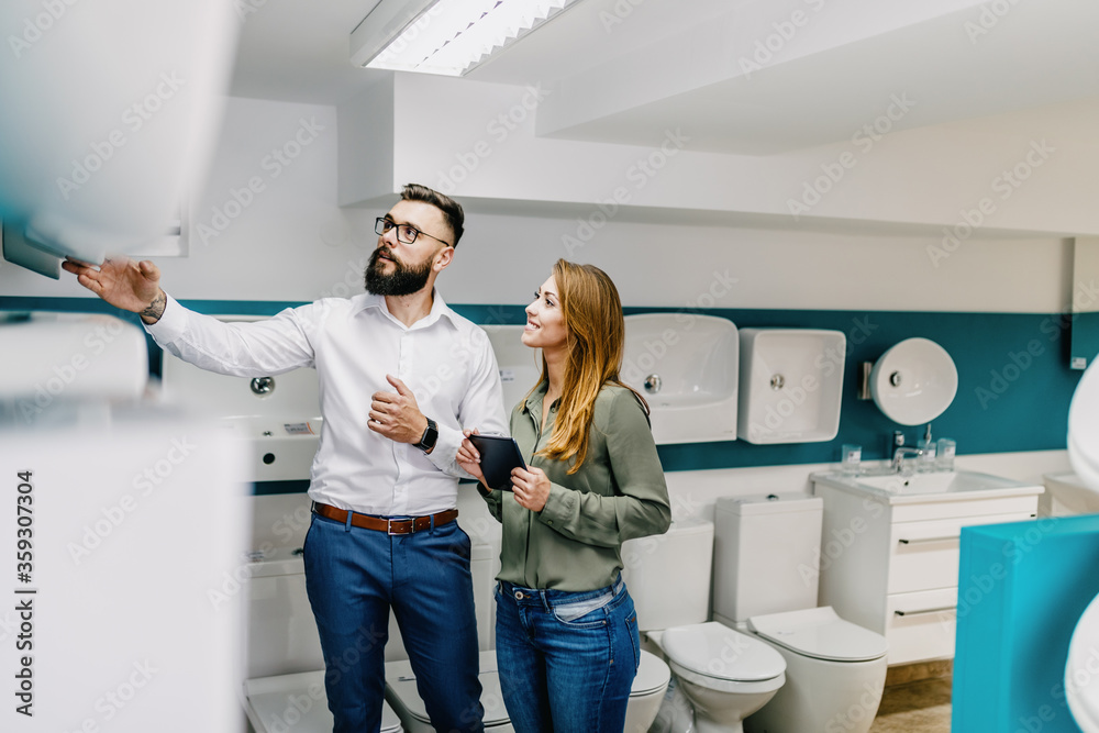 Obraz premium Middle age man choosing ceramic tiles and utensils for his home bathroom and female seller helps him to make right decision