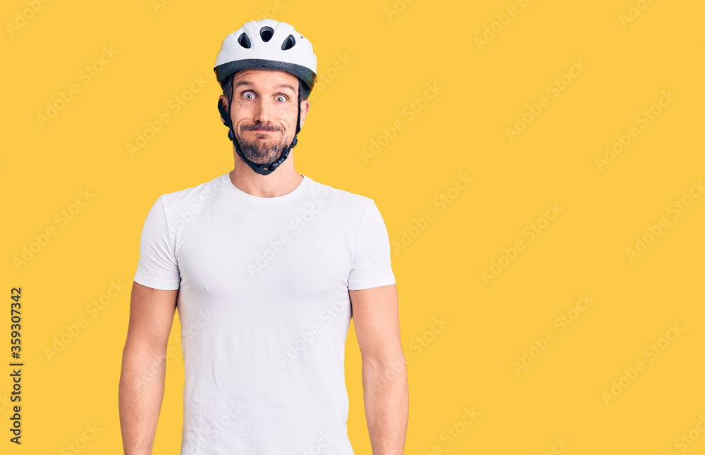 Young handsome man wearing bike helmet puffing cheeks with funny face. mouth inflated with air, crazy expression.
