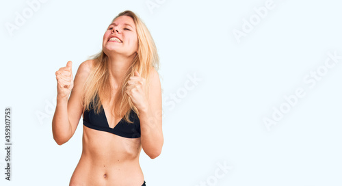 Young beautiful blonde woman wearing bikini excited for success with arms raised and eyes closed celebrating victory smiling. winner concept.