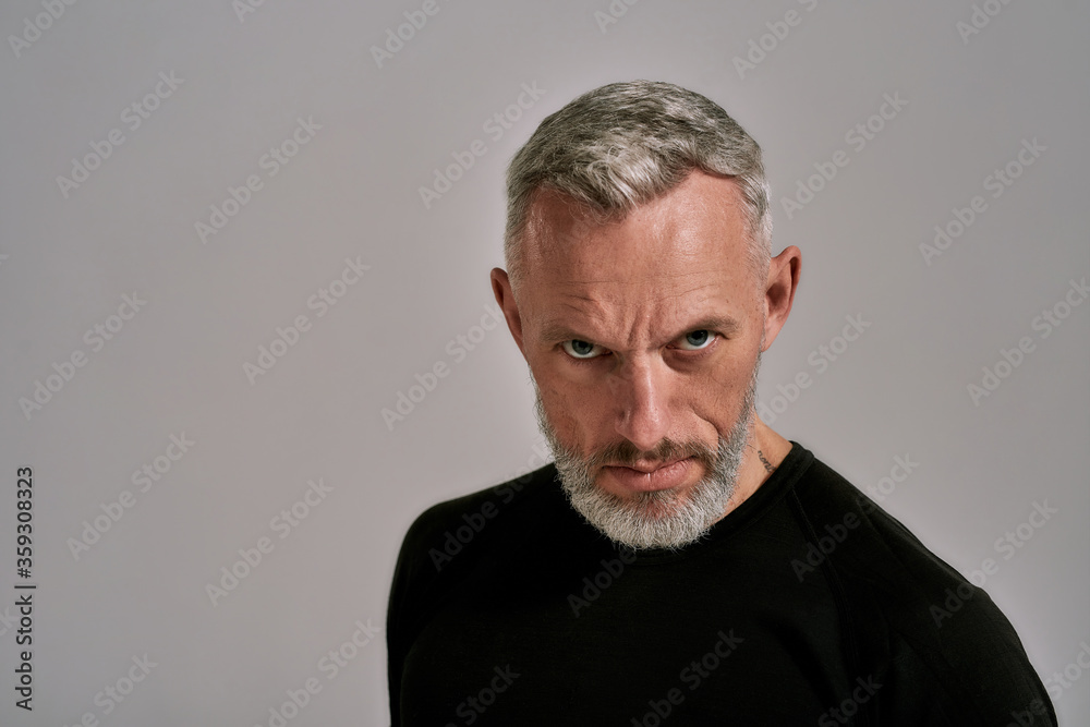 Close up of middle aged man in black t shirt looking at camera while posing in studio over grey background Close up of middle aged man in black t shirt looking at camera while posing in studio over grey background
