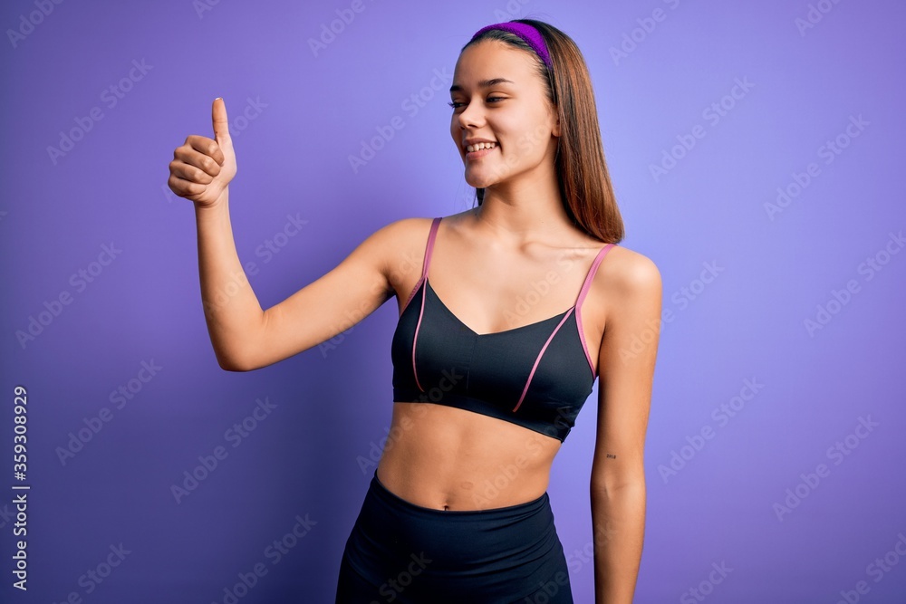 Young beautiful sporty girl doing sport wearing sportswear over isolated purple background Looking proud, smiling doing thumbs up gesture to the side Young beautiful sporty girl doing sport wearing sportswear over isolated purple background Looking proud, smiling doing thumbs up gesture to the side