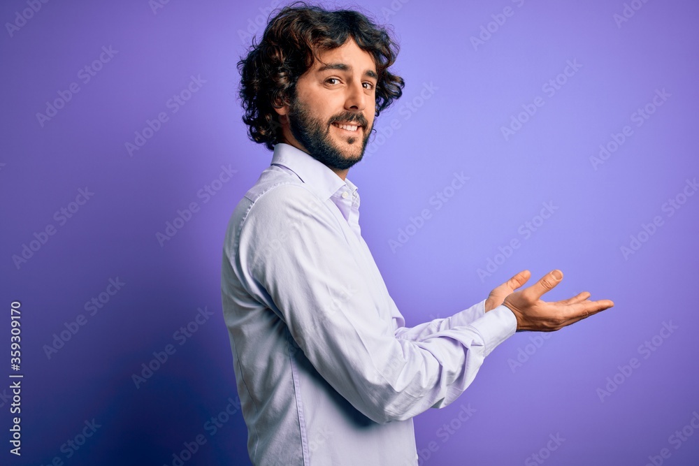 Young handsome business man with beard wearing shirt standing over purple background pointing aside with hands open palms showing copy space, presenting advertisement smiling excited happy