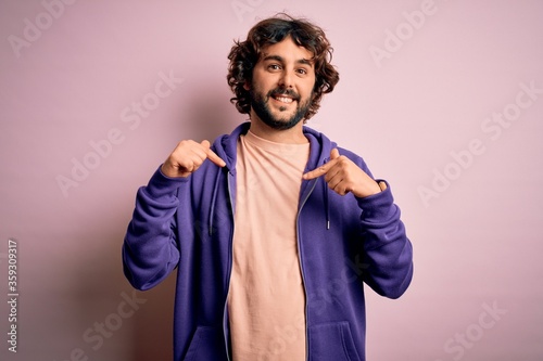 Young handsome sporty man with beard wearing casual sweatshirt over pink background looking confident with smile on face, pointing oneself with fingers proud and happy.