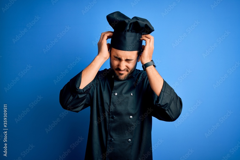 Young handsome chef man with beard wearing cooker uniform and hat over blue background suffering from headache desperate and stressed because pain and migraine. Hands on head. Young handsome chef man with beard wearing cooker uniform and hat over blue background suffering from headache desperate and stressed because pain and migraine. Hands on head.