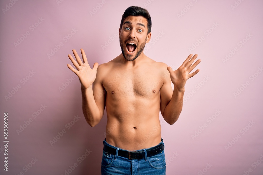 Young handsome strong man with beard shirtless standing over isolated pink background celebrating crazy and amazed for success with arms raised and open eyes screaming excited. Winner concept