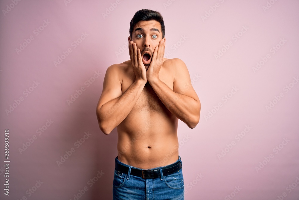 Young handsome strong man with beard shirtless standing over isolated pink background afraid and shocked, surprise and amazed expression with hands on face