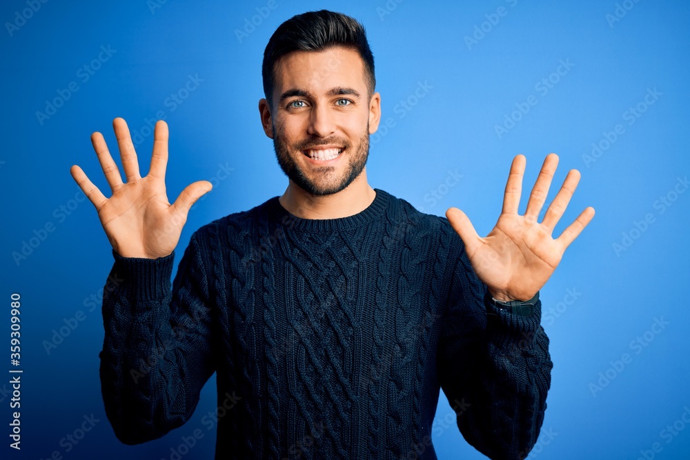 Naklejka premium Young handsome man wearing casual sweater standing over isolated blue background showing and pointing up with fingers number ten while smiling confident and happy.
