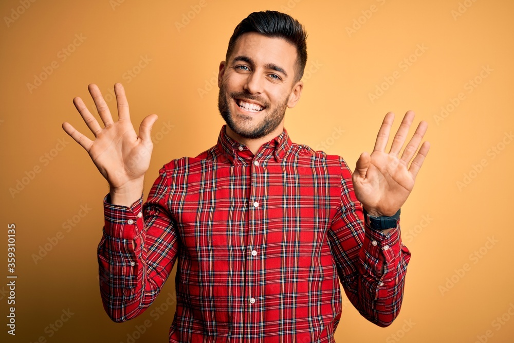 Young handsome man wearing casual shirt standing over isolated yellow background showing and pointing up with fingers number nine while smiling confident and happy. Young handsome man wearing casual shirt standing over isolated yellow background showing and pointing up with fingers number nine while smiling confident and happy.